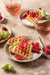 Homemade waffles with summer berries and yogurt served for sweet breakfast with tea on beige background. Heart shaped waffles