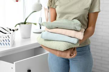 Beautiful young African-American woman putting clean clothes into commode at home, closeup