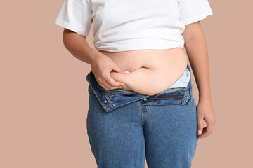 Overweight woman in tight jeans on beige background. Excess weight concept