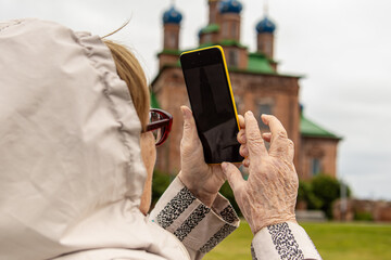 An elderly woman takes pictures on phone. An elderly woman traveler. The Orthodox church in background