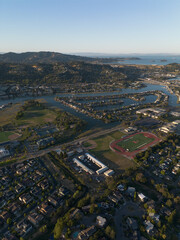 Arial wide of town with river running through along bay, lots of blue water and green trees, golden hour sunset shining