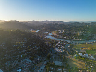 Arial wide of town with river running through, lots of blue water and green trees, golden hour...