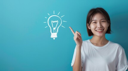 A young woman smiles and points to a lightbulb drawn on a blue wall