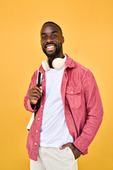 Smiling cool generation z Black student guy wearing backpack headphones posing for portrait. Happy young adult African man hipster standing isolated on yellow background looking at camera. Vertical