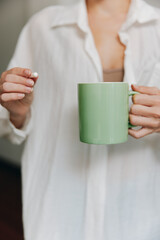 Woman in white shirt holding green coffee mug and pill in hand, closeup shot