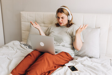 Shocked concerned user in headphones looking at laptop screen, finding problems with online app,...