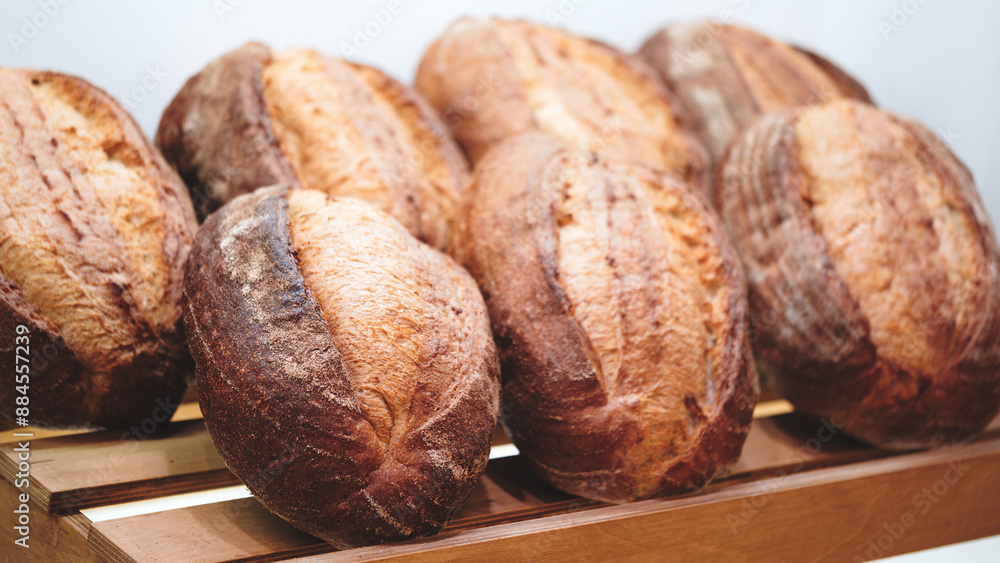 Poster a row of bread loaves are on a wooden shelf. the loaves are all different sizes and shapes, but they