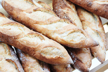 A row of bread loaves are on a wooden shelf. The loaves are all different sizes and shapes, but they all have a similar appearance. The bread looks fresh and inviting