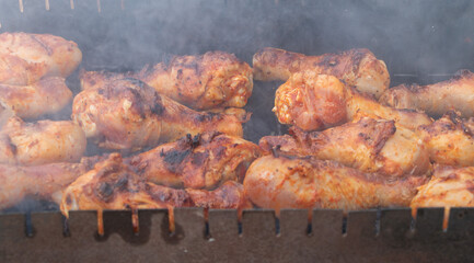 close up of chicken wings and legs on the grill, smoke coming from under them,