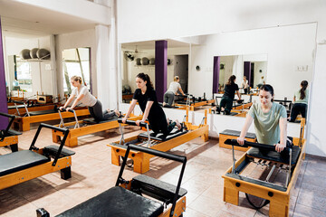 Group of young women exercising on reformer pilates bed.