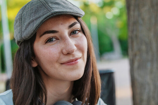 Young woman in a cap smiling at the camera outdoors