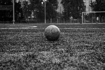 Old dirty ball on green soccer field.
Team sport, football match at the stadium.
Black and white photo