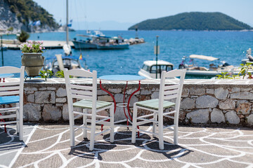 White chairs and a blue table overlooking a sunny harbor in Greece