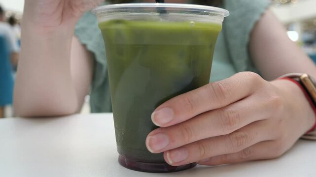ice green tea matcha. Woman stirring ice matcha cocktail at a restaurant. Concept of heat and cold drink, quenching thirst.