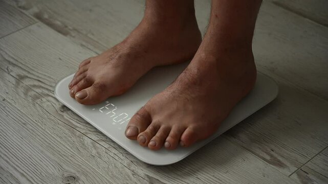 A Caucasian barefoot obese man weighs himself on an electronic scale. Close-up of a man's feet. 