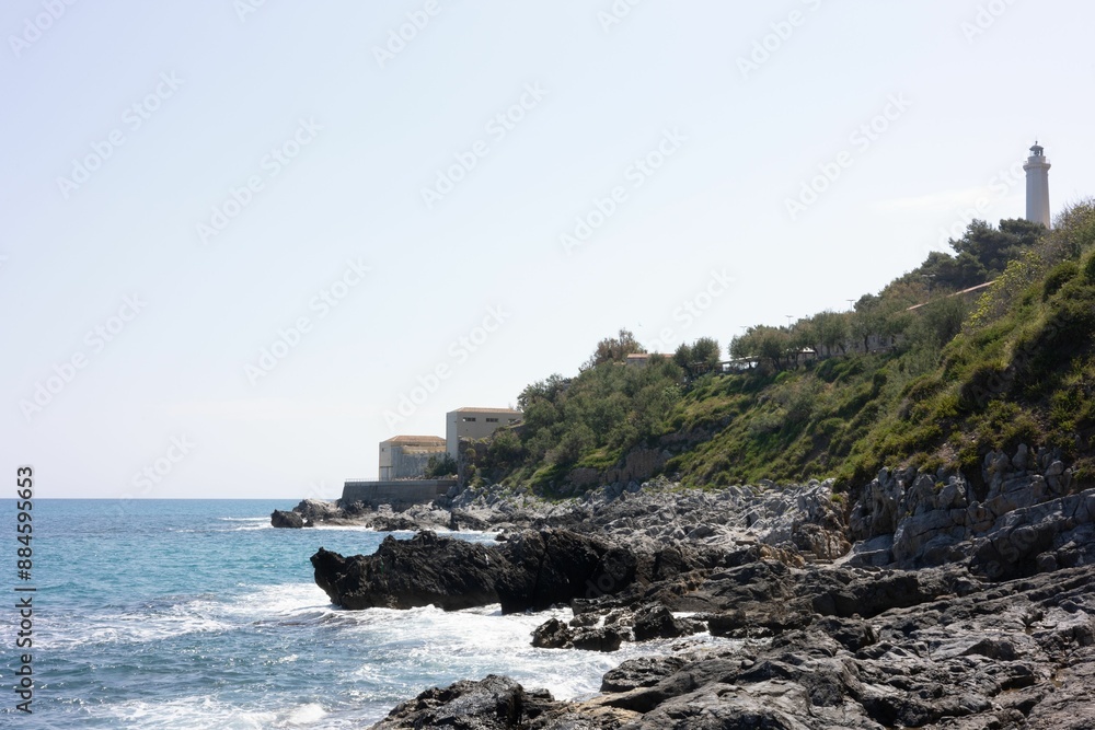 Sticker Rocky coastline with a lighthouse and buildings overlooking the sea under a clear sky