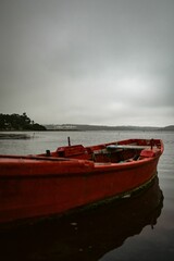 Fototapeta premium Red wooden boat floating on a calm lake under an overcast sky