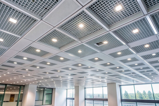 Interior modern building of Office ceiling in perspective with white texture of acoustic gypsum plasterboard, lighting fixtures or fluorescent panel light suspended on square grid structure.