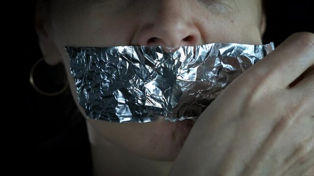 Woman takes off sticky tape. A woman takes off the sticky tape from the mouth to start speaking about violence.