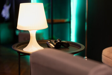 Gaming console controller sitting on nightstand in neon illuminated living room. Game system...