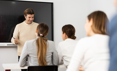 Fototapeta premium Male business coach explaining topic while standing against group of people sitting at desks in front of him