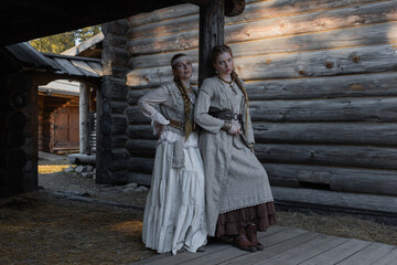 Naklejka premium Young girls in folk costumes, in a village among wooden architecture, Slavic or Nordic style
