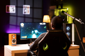 African american man playing SF space videogame on PC screen in neon illuminated apartment living...
