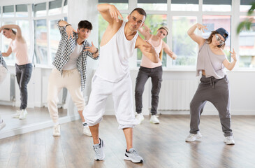 Active young guy practicing basic hip-hop moves in training hall during dancing classes