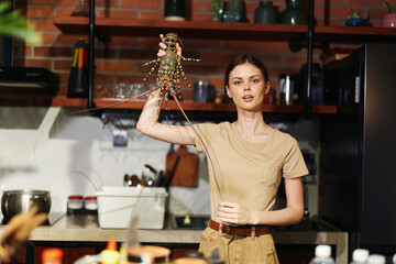 Woman holding live lobster in hands standing in front of kitchen counter, preparing to cook seafood dish
