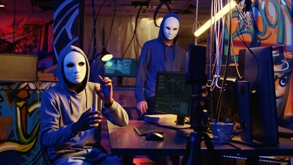 Hacker group wearing anonymous masks filming video threatening another country government to steal military secrets, doing international espionage in hidden underground base