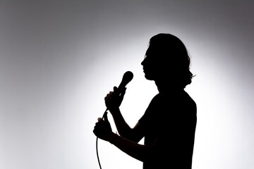 Silhouette of young singer holding wired microphone and singing with emotion.