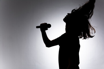 Silhouette of young man holding wireless microphone singing music with emotion.