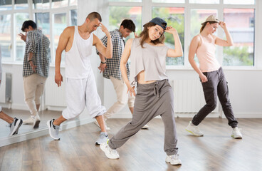 Fototapeta premium Girl makes movements and teaches group of hip hop fans to move beautifully and confidently to music, to control their bodies. Young boys and girl repeat after teacher