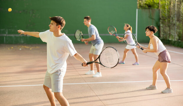 Sporty young Argentinian guy playing popular team game frontenis at open-air fronton court on summer day, ready to hit rubber ball with racquet
