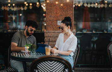 Two colleagues having a business meeting in an outdoor coffee shop, discussing work on a tablet.