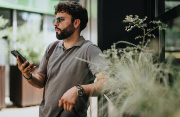 A business person standing outdoors, holding a smart phone and looking thoughtful, surrounded by greenery. Captures a moment of contemplation.