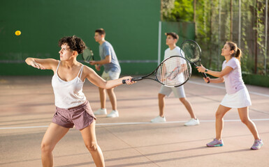 Concentrated young hispanic female frontenis player swinging string racquet to hit ball on outdoor...