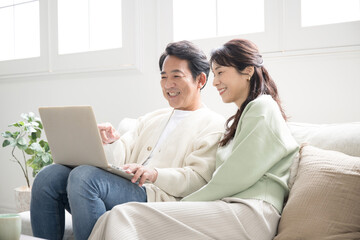 Fototapeta premium Smiling middle-aged couple in their 50s searching for a computer to look at