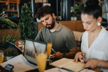 Two businesspeople working intently on their laptops and notes at a coffee bar, collaborating on a project