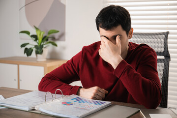 Embarrassed man covering face with hand at table in office