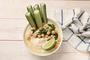 Tasty hummus with chickpeas, cucumber and lime in bowl on wooden table, top view