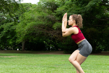 Latin woman in active wear meditating during yoga session in the nature public park. Garudasana eagle posture.