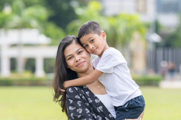 Fototapeta premium A 30-something Indian Malaysian mother joyfully playing on the expansive lawn at Merdeka Square in Kuala Lumpur, Malaysia, while holding her 7-year-old son.