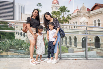Obraz premium Two 30-something Indian Malaysian mothers with their 7-year-old son and 5-year-old daughter spending time joyfully on a bridge in City Centre, Kuala Lumpur, Malaysia.