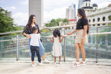 Fototapeta premium Two 30-something Indian Malaysian mothers with their 7-year-old son and 5-year-old daughter spending time joyfully on a bridge in City Centre, Kuala Lumpur, Malaysia.