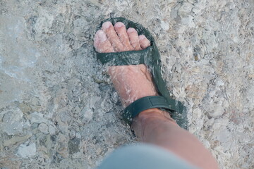 A woman's foot wearing sandal in the water of a white sandy beach