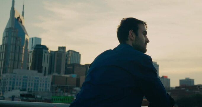Young man standing on a bridge looking out at the sunset