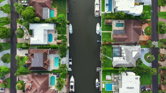 Florida luxury waterfront homes with private pools and yachts docked along a canal. Aerial top down shot above multi-million dollar mansions.