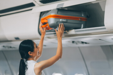 Young Female Tourist Storing Luggage in Overhead Compartment on Airplane During Travel