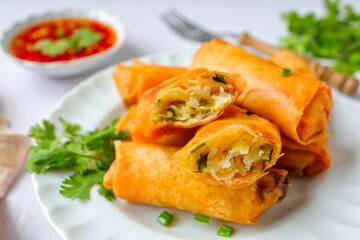 Deep fried vegetable spring rolls or egg rolls and sauce , Thai called popia, in white plate on a white table background with fork
